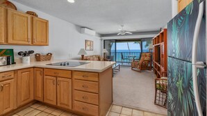 A kitchen with wooden cabinets, a large island, and a view of the ocean through the sliding glass door. - Big Island Kona Isle E32 1 Bedroom Condo (Kailua-Kona)
