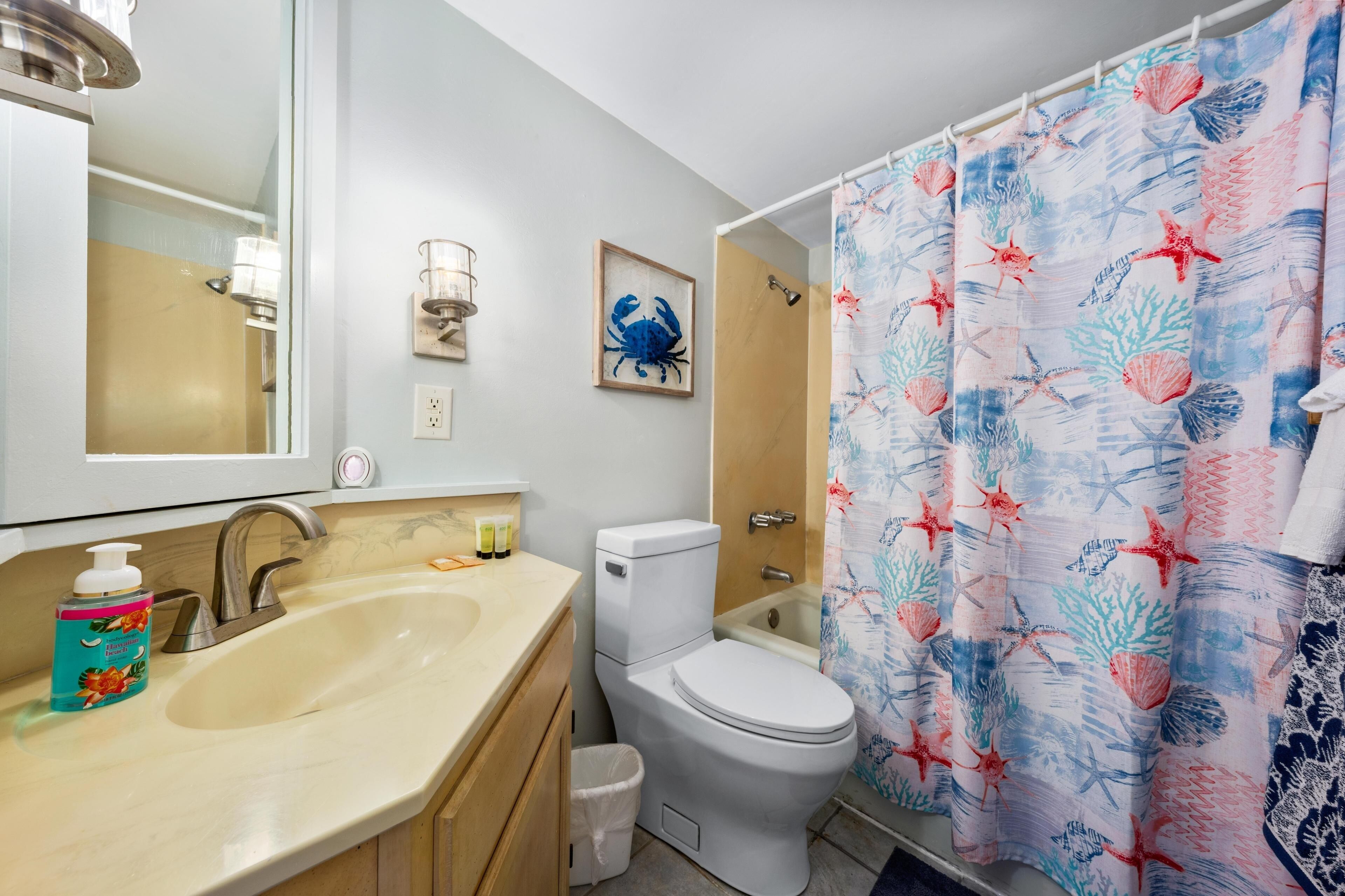 Baño con lavamanos, inodoro y cortina de ducha con motivos marinos.