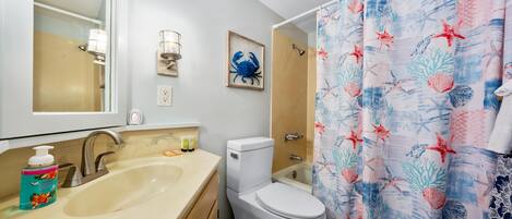 Baño con lavamanos, inodoro y cortina de ducha con motivos marinos.