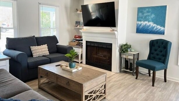 A modern living room with a fireplace, a television mounted above it, a ceiling fan, and a large window. - 604 Wedgewood 3 Bedroom Home (North Myrtle Beach)