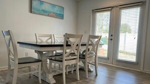A dining area with a table and four chairs, a painting on the wall, and a sliding glass door leading outside. - 604 Wedgewood 3 Bedroom Home (North Myrtle Beach)