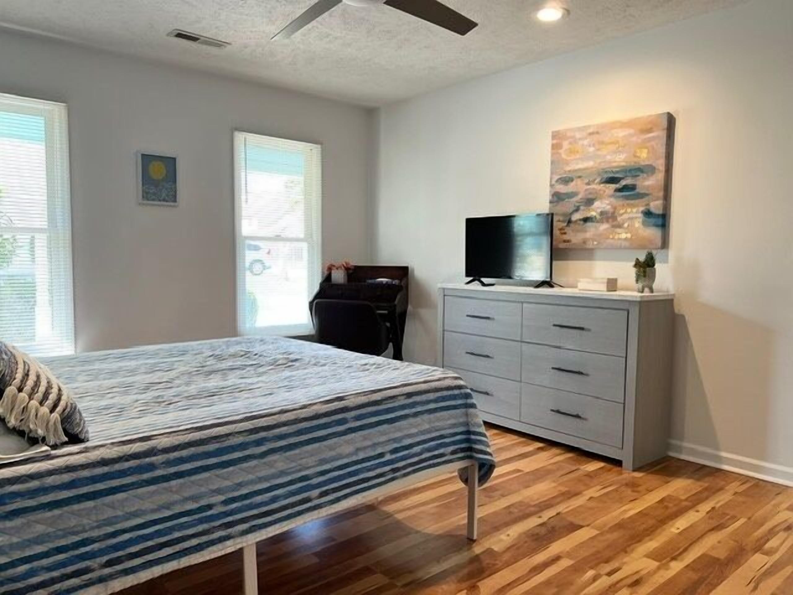 A bedroom with a bed, a dresser, a television, and artwork on the wall.