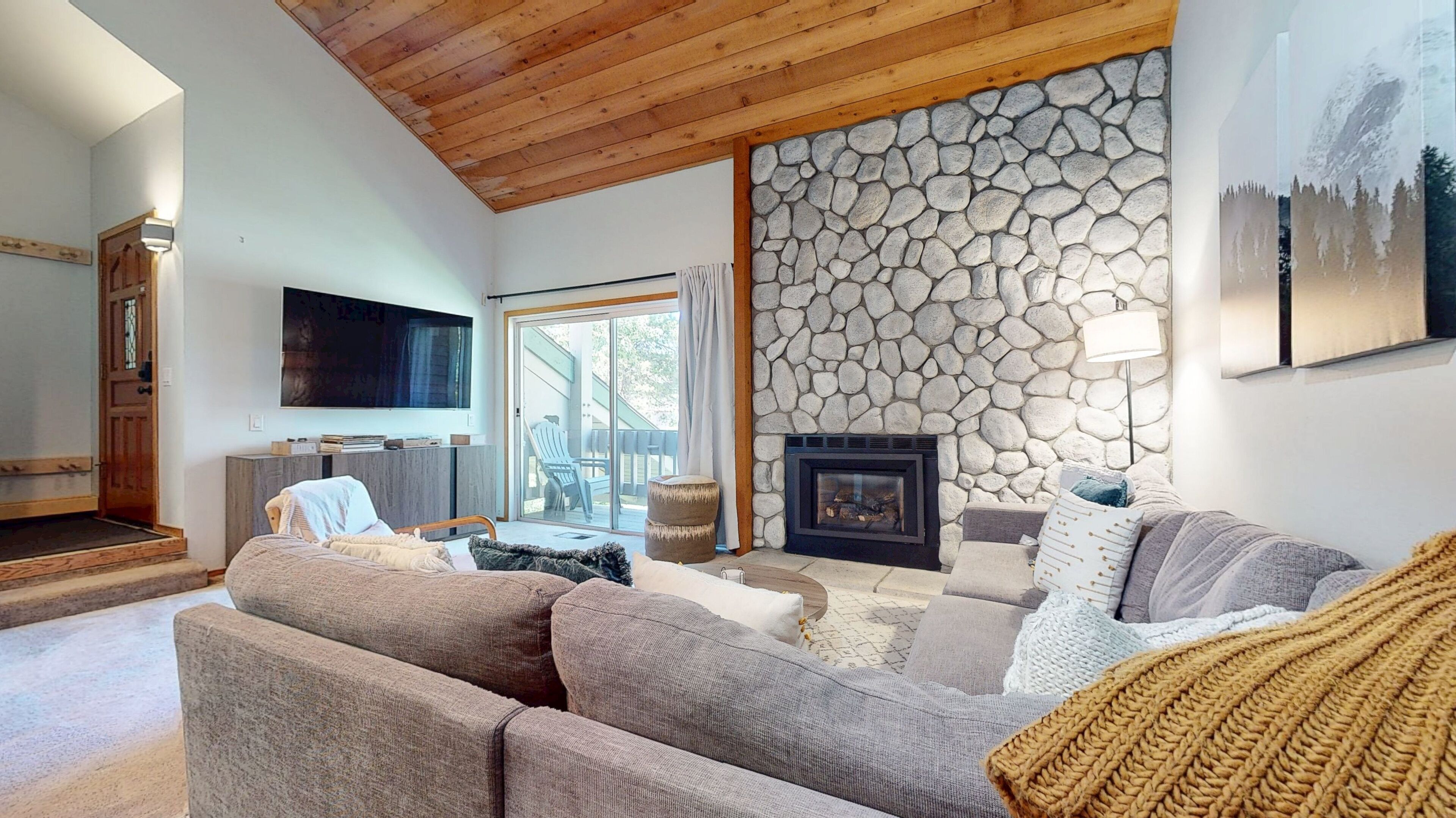 A cozy living room with a stone fireplace, a comfortable sofa, and a television mounted on the wall.