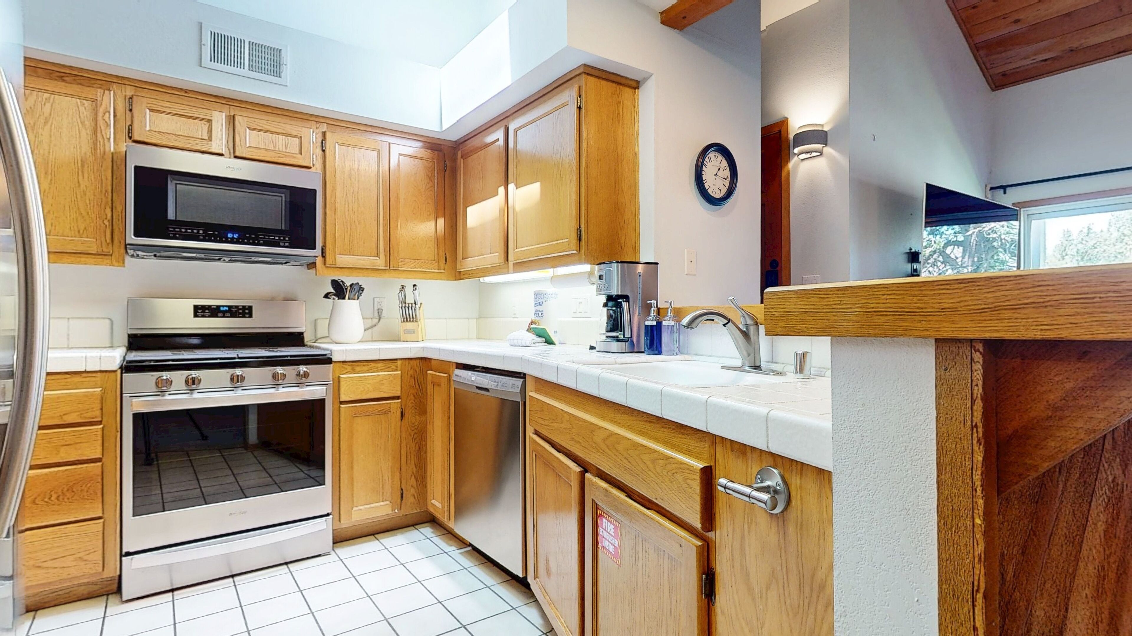 A compact kitchen with wooden cabinets, a microwave, stove, and a dishwasher.
