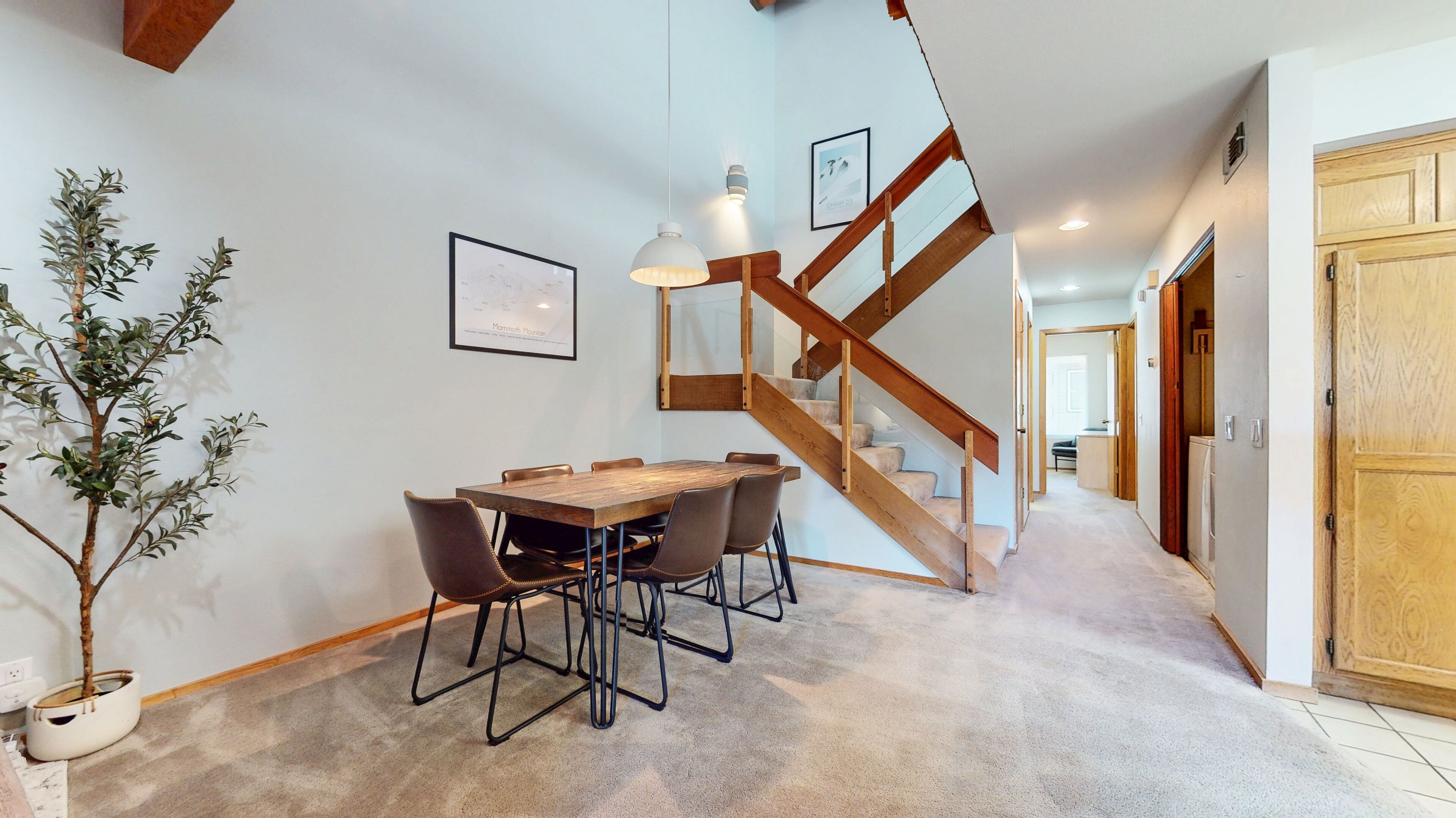 A dining area with a wooden table and chairs, a staircase, and a potted plant.
