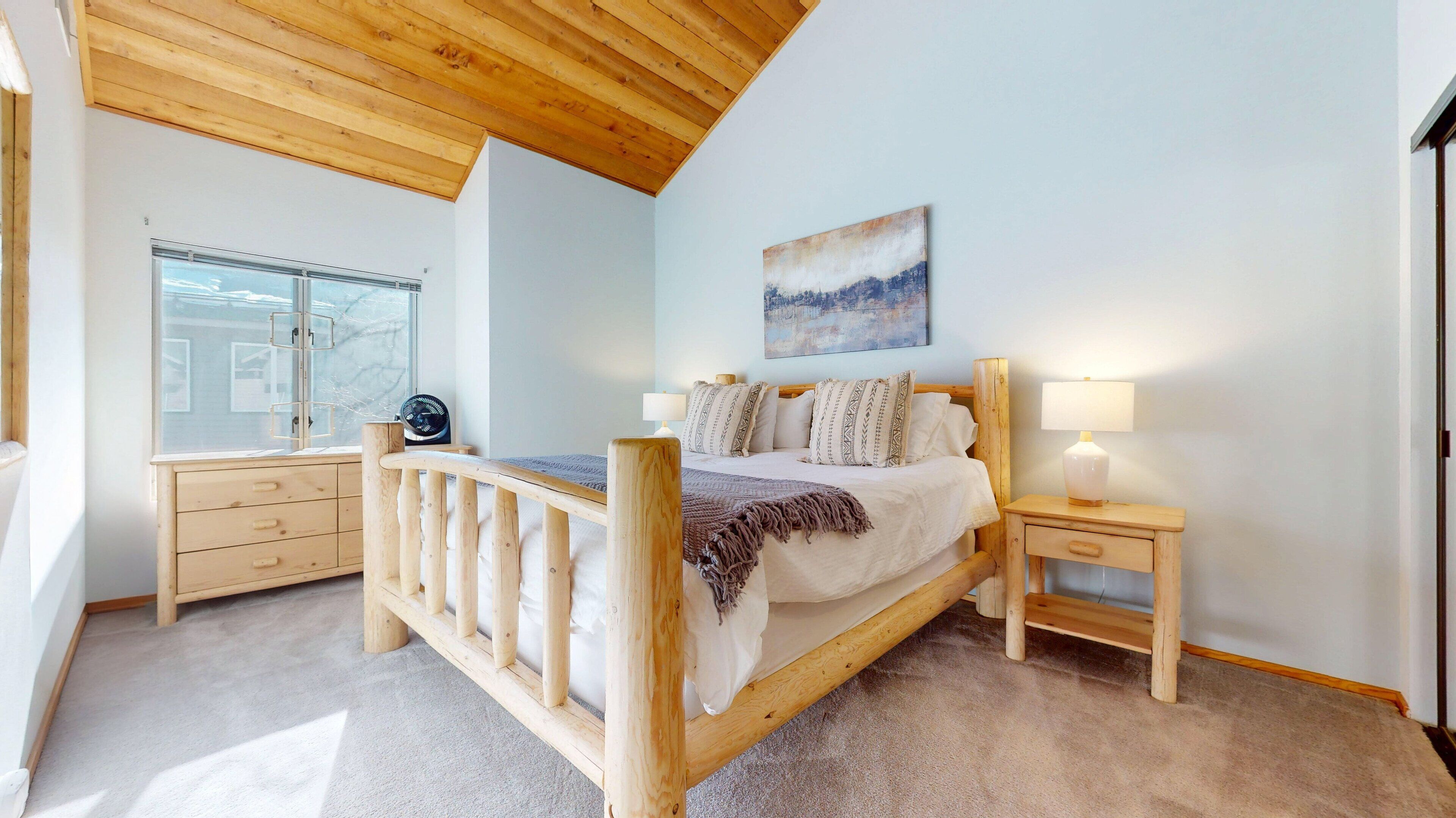 Una camera da letto con un letto di legno, un comodino con una lampada, una finestra vista e un quadro appeso al muro.