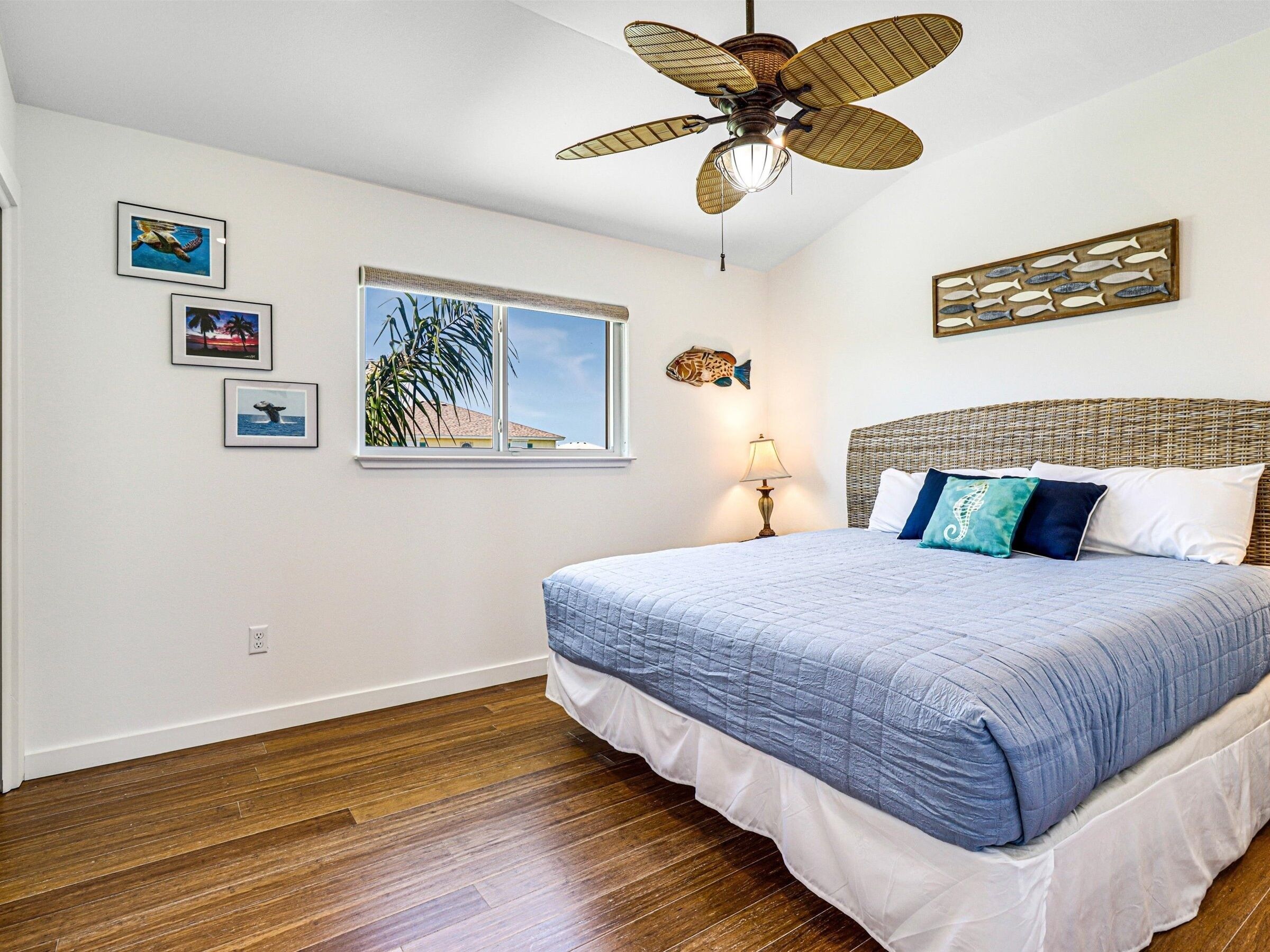 A bedroom with a bed, a ceiling fan, a window with a view, and wall art.