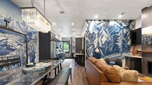 Een moderne woonkamer met een groot muurschildering van een besneeuwd berglandschap, een glazen salontafel met boeken, een leren bank en een open haard.