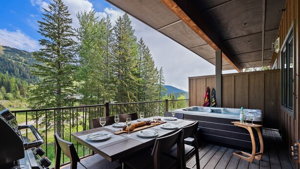 Een houten terras met een eettafel voor vier personen, een jacuzzi en een barbecue.