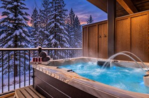Een hottub op een houten terras met besneeuwde bomen op de achtergrond.