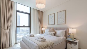 Een moderne hotelkamer met een groot bed, een nachtkastje met lamp en uitzicht op de stad door middel van kamerhoge ramen.
