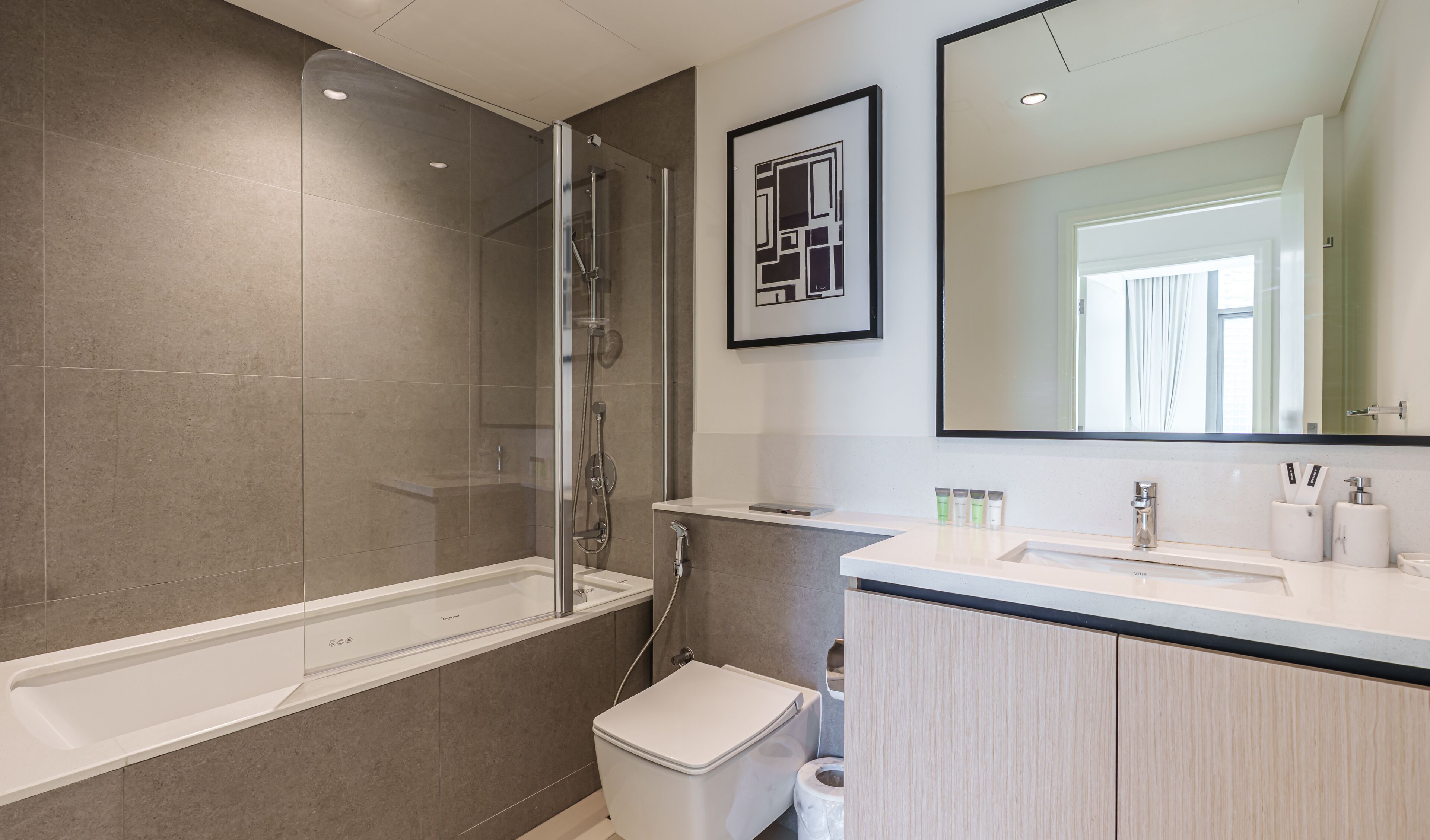 A modern bathroom with a glass-enclosed shower, a white bathtub, a toilet, and a vanity with a mirror.