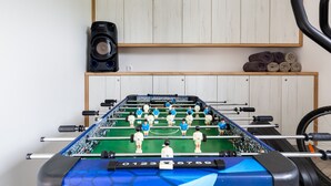 Een tafelvoetbaltafel met een blauw en groen speelveld, een speaker aan de muur en een fietswiel op de voorgrond.