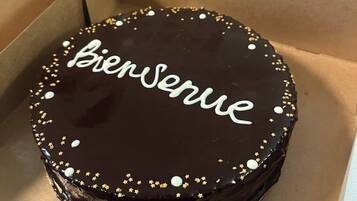 A round chocolate cake with "Bienvenue" written on top, decorated with small white and gold edible decorations.
