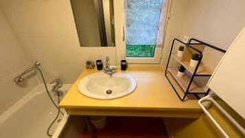 A bathroom with a bathtub, a sink, and a window with a view of greenery.