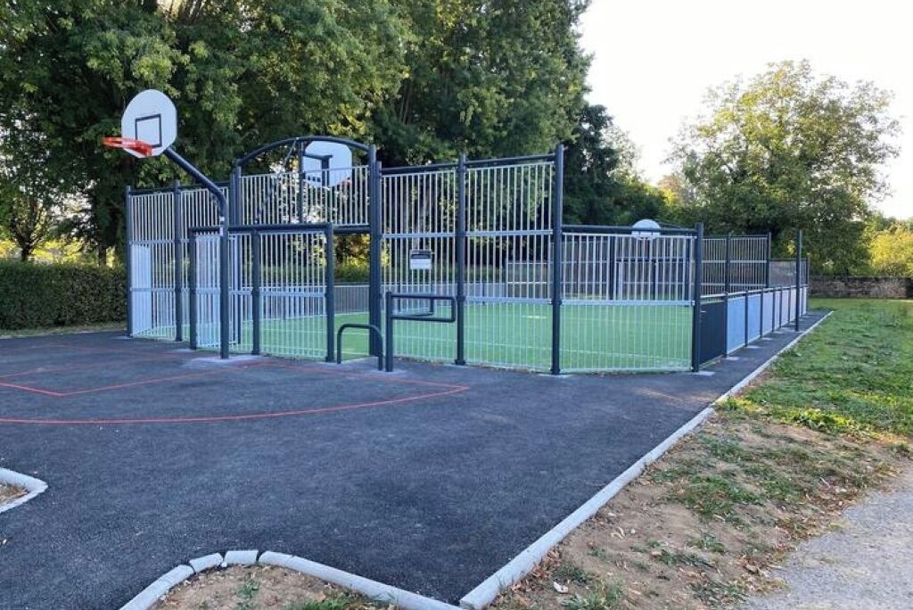Un patio de juegos con aro de baloncesto, estructuras para escalar y una zona vallada.