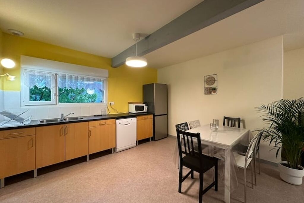 A compact kitchen with a microwave, refrigerator, and dishwasher. There is a dining table with chairs and a potted plant.
