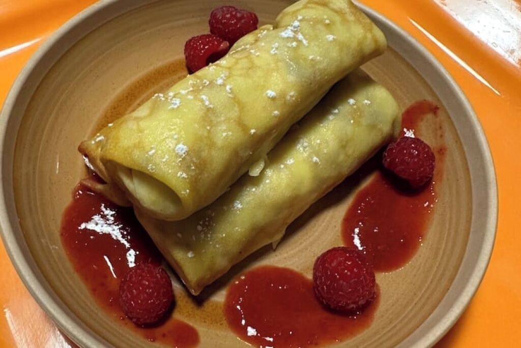 Een bord met twee rolkoekjes, frambozensaus en frambozen.