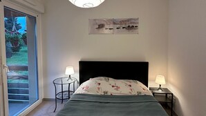 A bedroom with a bed, a nightstand, a table lamp, a wall art piece, and a view of a garden through a sliding door.