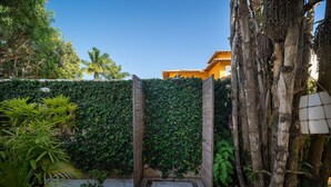 A garden with a wooden gate, a concrete pathway, and various plants. - Bz92 Casa 600m Rua das Pedras 4 suítes (Buzios)