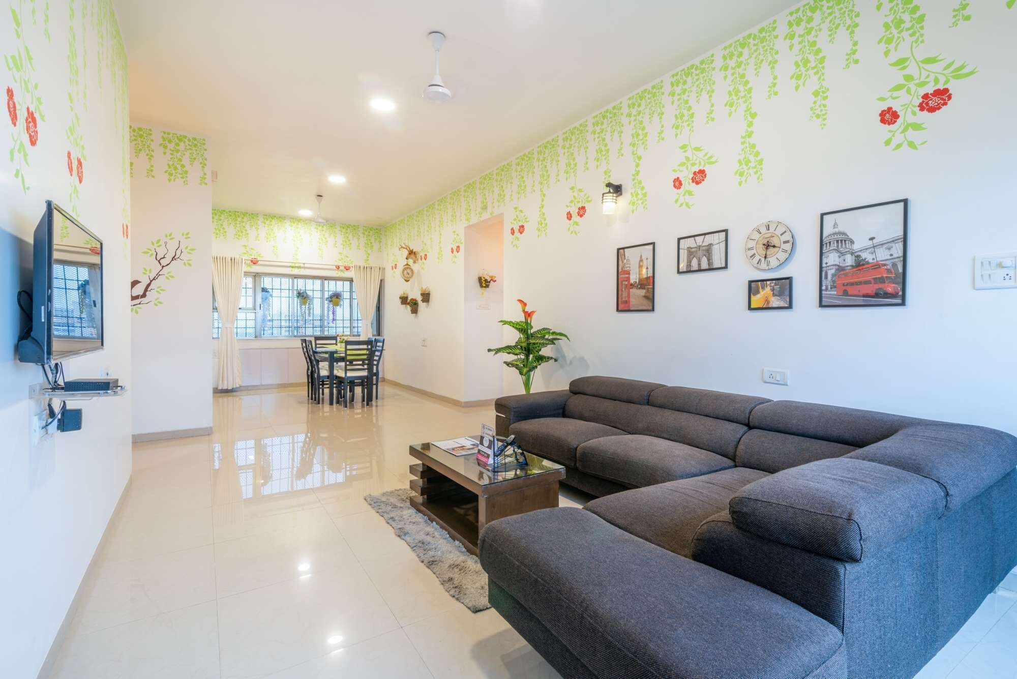 A modern living room with a grey sectional sofa, a dining table with chairs, and a TV mounted on the wall.
