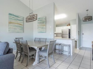 Un coin repas avec une table et des chaises, une cuisine en arrière-plan et une porte sur la droite.
