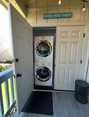 A laundry room with two front-loading washing machines, a door with a sign above it, and a small trash bin to the right.