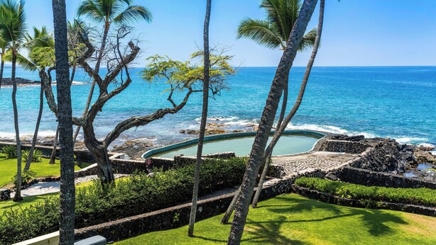 A tropical resort with a pool, palm trees, and a view of the ocean. - Summer Deal Oceanfront Kona 1BR Condo with Pool and Beach Access (Kailua-Kona)