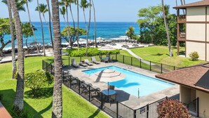 A pool area with lounge chairs and umbrellas, surrounded by palm trees and a view of the ocean. - Summer Deal Oceanfront Kona 1BR Condo with Pool and Beach Access (Kailua-Kona)