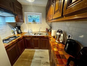 A kitchen with wooden cabinets, a gas stove, a sink, and a window with a view of greenery.