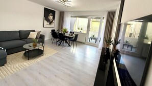 Una sala de estar moderna con un sofá gris, una mesa de comedor para cuatro personas y una gran pantalla de televisión.