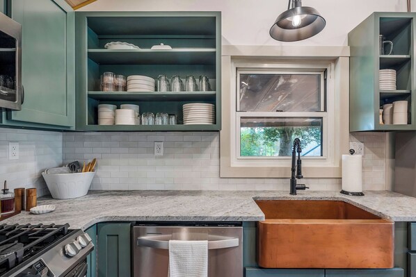 A kitchen with teal cabinets, a stainless steel dishwasher, and a copper sink.
