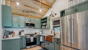 A modern kitchen with teal cabinets, stainless steel appliances, and a wooden ceiling. - Charming 3-bed 3-bath, country cottage, fully renovated, on the edge of town. (Sparta)