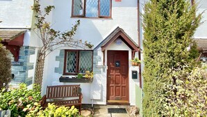 A two-story house with a white exterior, a brown front door, and a small porch with a bench. - Padstow Holiday Home 2 Bedrooms, wifi, rear decked patio, pets welcome - parking (Padstow)