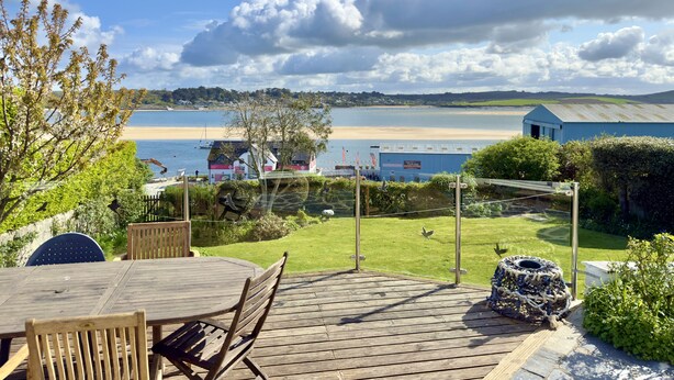 A wooden deck with a table and chairs overlooking a beach and a body of water.