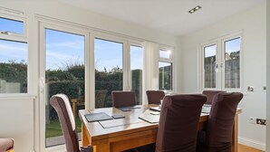 Un'area da pranzo con un tavolo di legno e sei sedie, ampie finestre e vista sul giardino.