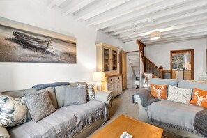 A cozy living room with a sofa, a coffee table, a cabinet, and a painting of a boat.