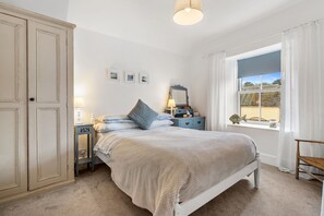 A bedroom with a bed, bedside tables, a wardrobe, a window with curtains, and a lamp.