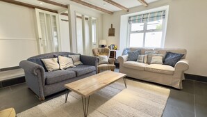 A spacious living room with two sofas, a coffee table, and a large window providing natural light. - 36 High Street -  a two storey property that sleeps 6 guests  in 3 bedrooms (Padstow)