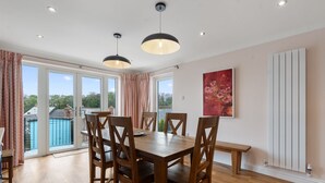 A dining area with a wooden table and chairs, large windows, and a view of a swimming pool.