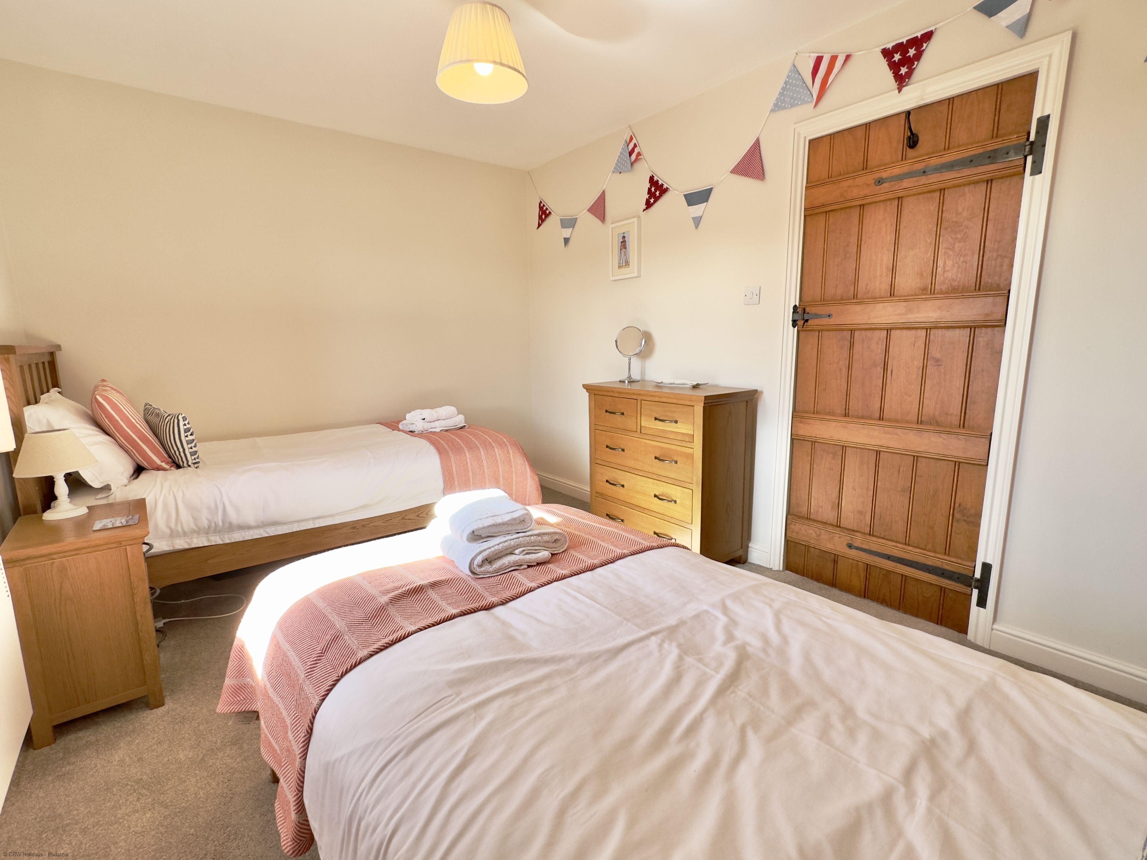 A bedroom with two single beds, a wooden dresser, a mirror, and a wardrobe with a sliding door.