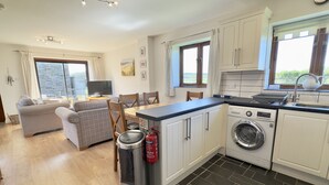 A compact kitchen with a washing machine, a dining area with a sofa and chairs, and a large window providing natural light.