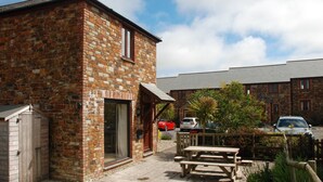 A brick building with a patio area, a wooden bench, and a car parked nearby.