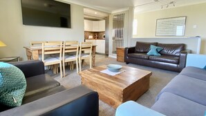 A living room with a brown leather sofa, a blue armchair, a wooden coffee table, and a dining area with wooden chairs and a table.