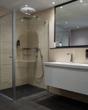Un baño moderno con ducha envuelta en vidrio, tocador blanco con espejo y piso de baldosas.