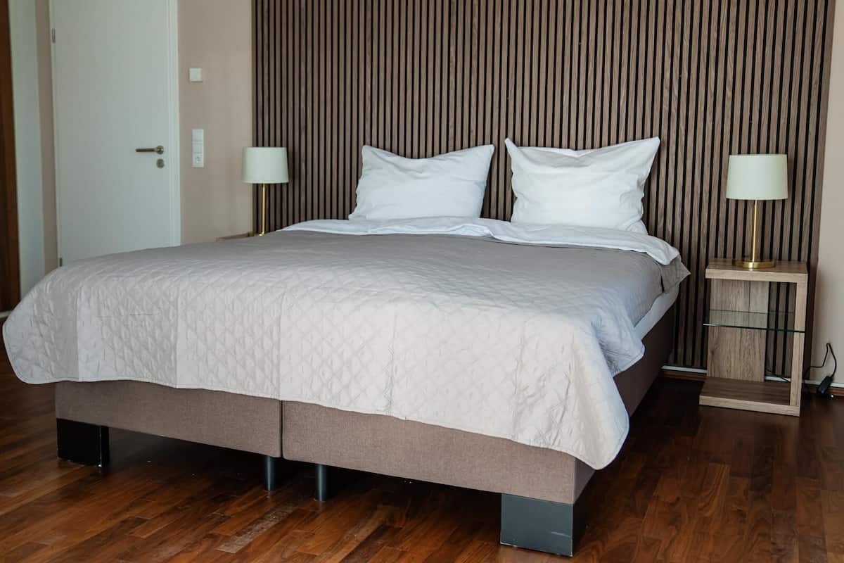 A neatly made bed with a quilted cover, two bedside lamps, and a wooden headboard.