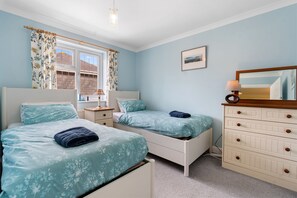 A bedroom with two beds, a dresser, a nightstand, and a window with curtains.