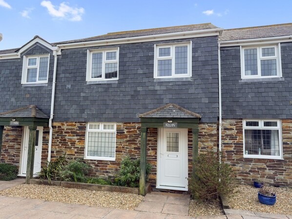 A row of terraced houses with stone and slate exteriors, white-framed windows, and a gravel front garden.