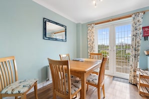 A dining area with a wooden table and chairs, a mirror on the wall, and a sliding glass door leading to an outdoor area.