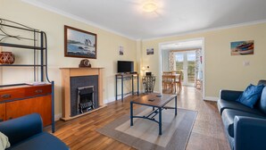 A living room with a fireplace, a television, a dining area, and a view through a glass door. - Kegyn - Harlyn Bay Cornwall,  sleeps 5 guests & accepts pets (Harlyn Bay)